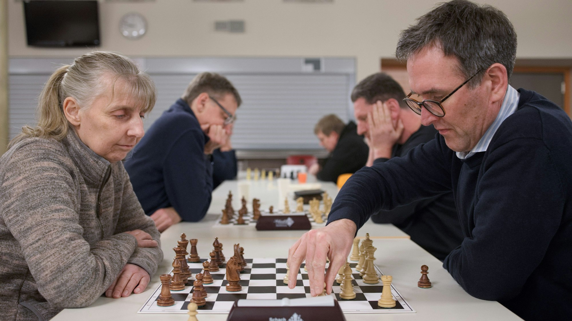 Konzentriert sitzen sich Schachspielerinnen und Schachspieler gegenüber, in der Mitte vor ihnen das Spielbrett mit den Figuren.