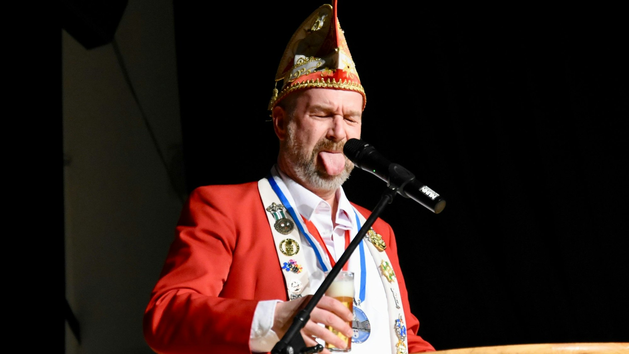 Ein Mann mit Narrenkappe streckt die Zunge heraus.