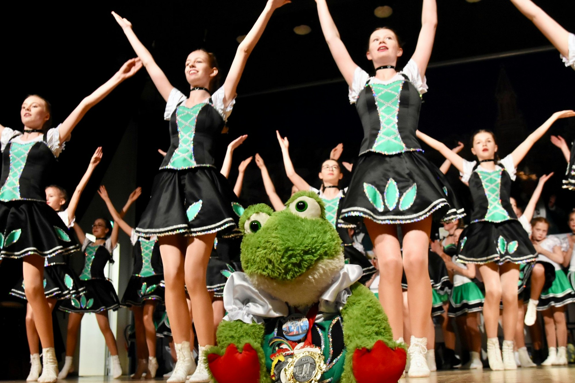 Junge Mädchen in grün-schwarzen Kostümen tanzen auf einer Bühne.