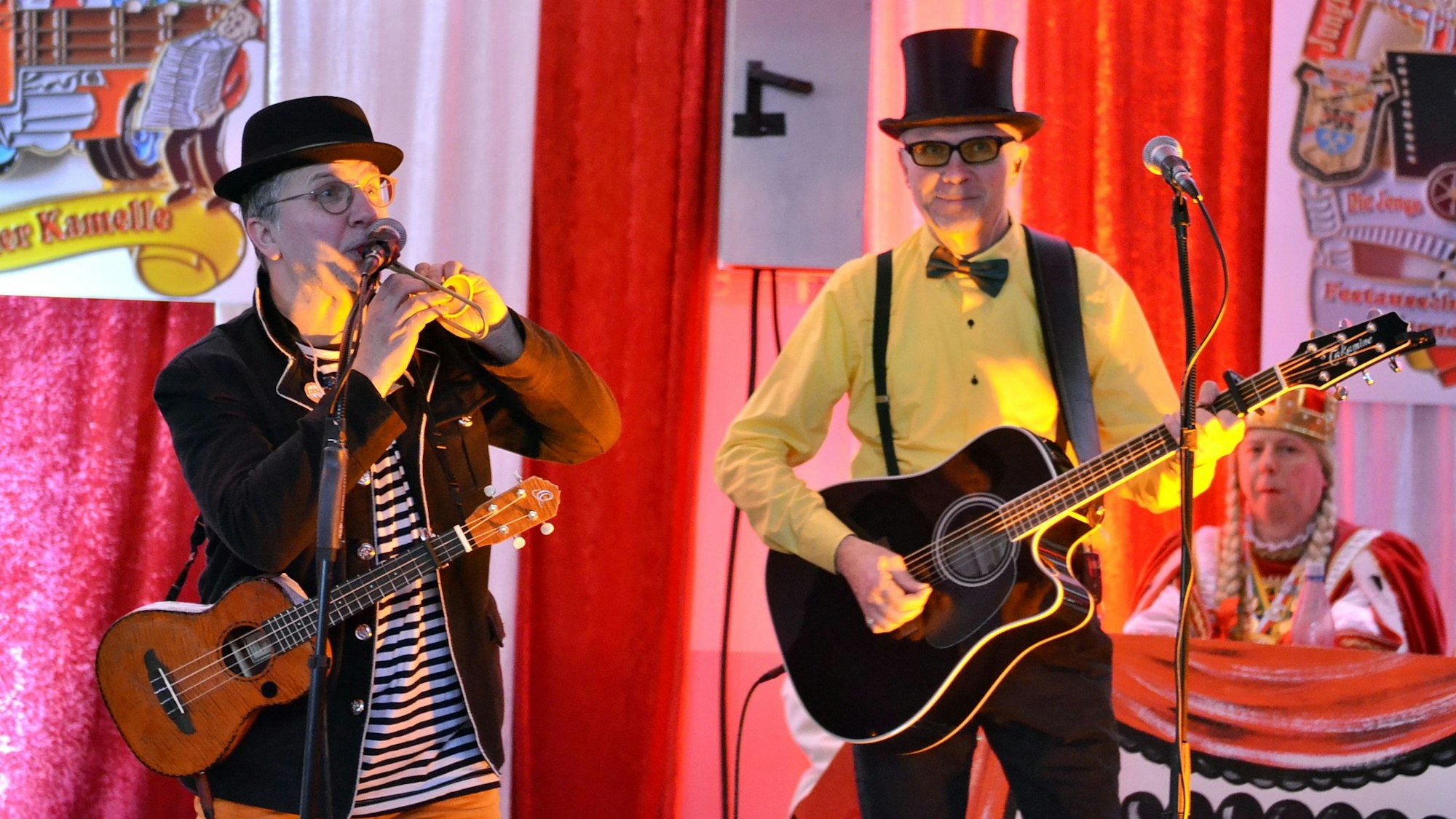 Zwei Karnevalisten mit Gitarren machen Musik. Im Hintergrund ist die Jungfrau des Dreigestirns zu sehen.