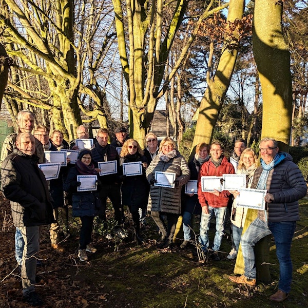 Auf dem Bild ist eine Gruppe von Menschen in einem Wald zu sehen, die Urkunden in den Händen hält.