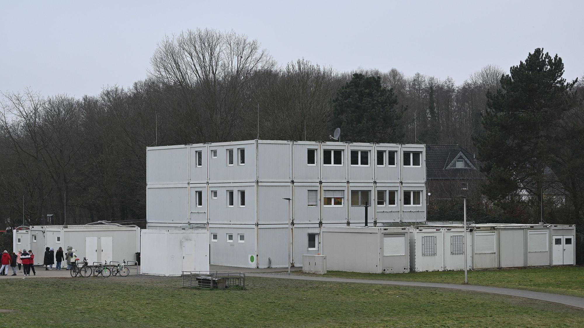 Ein dreistöckiger grauer Containerbau steht auf einer Wiese.