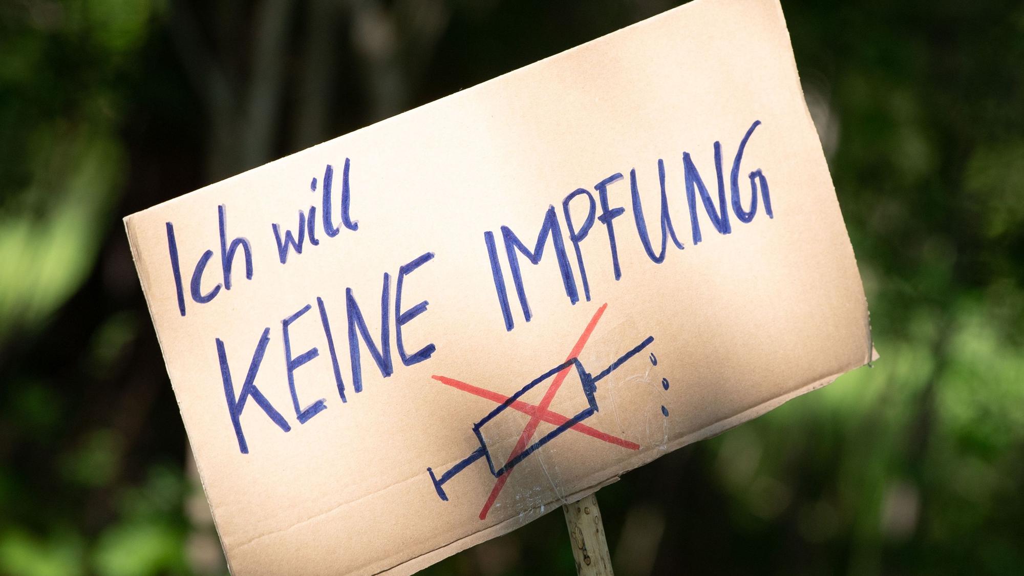 Ein Schild mit der Aufschrift «Ich will keine Impfung» steht am Rande einer Kundgebung von Anhängern von Verschwörungstheorien zur Corona-Krise im Großen Garten auf einer Wiese.