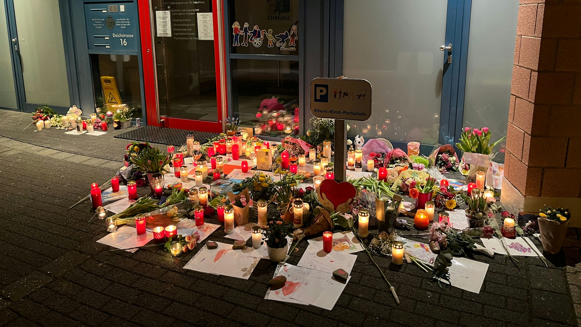 Vor der Tür einer Praxis liegen unzählige Kinderzeichnungen und leuchten zahlreiche Kerzen.