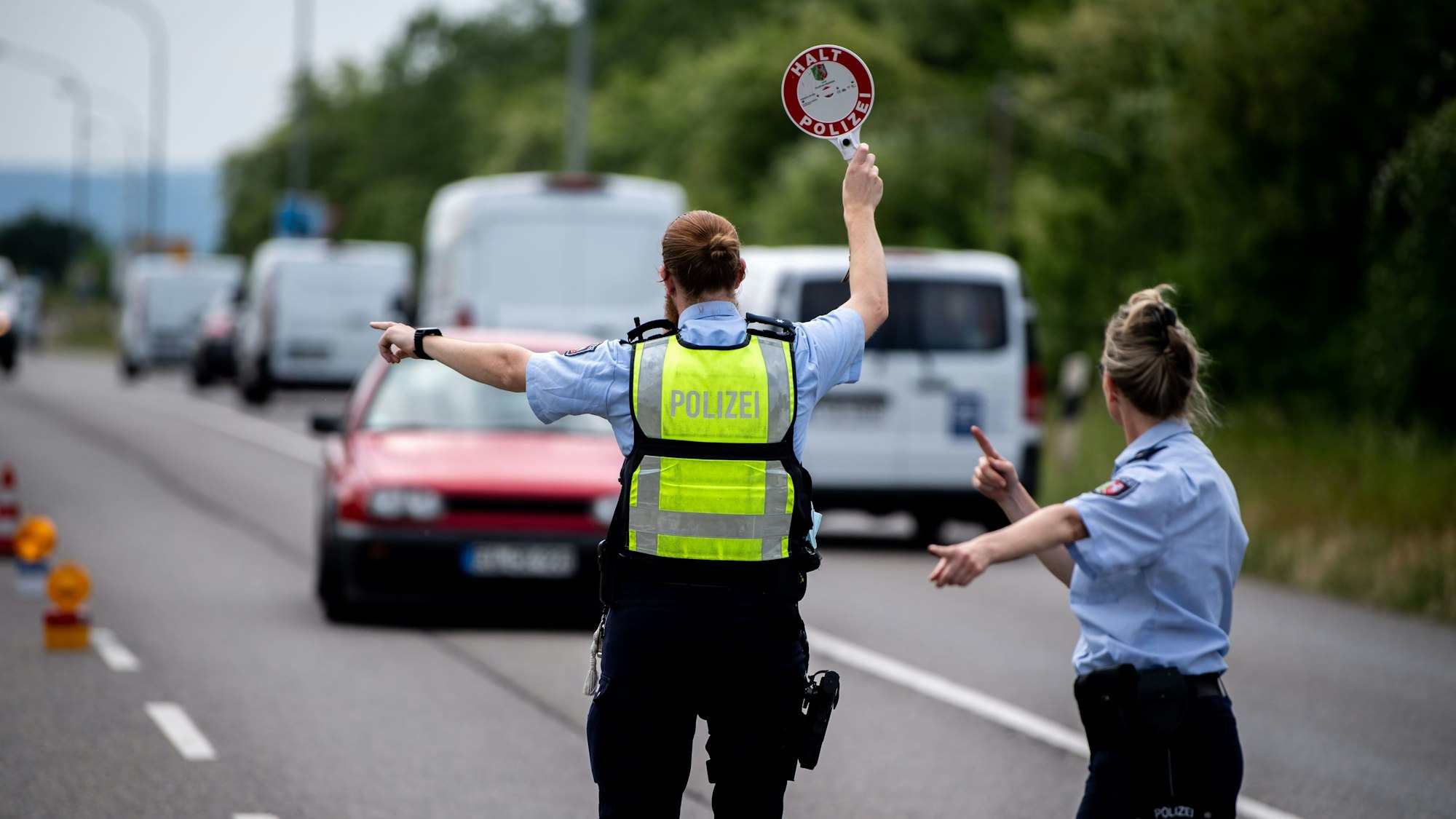Das Symbolbild zeigt einen Polizisten und eine Polizistin, die im Rahmen einer Verkehrskontrolle ein Auto stoppen.