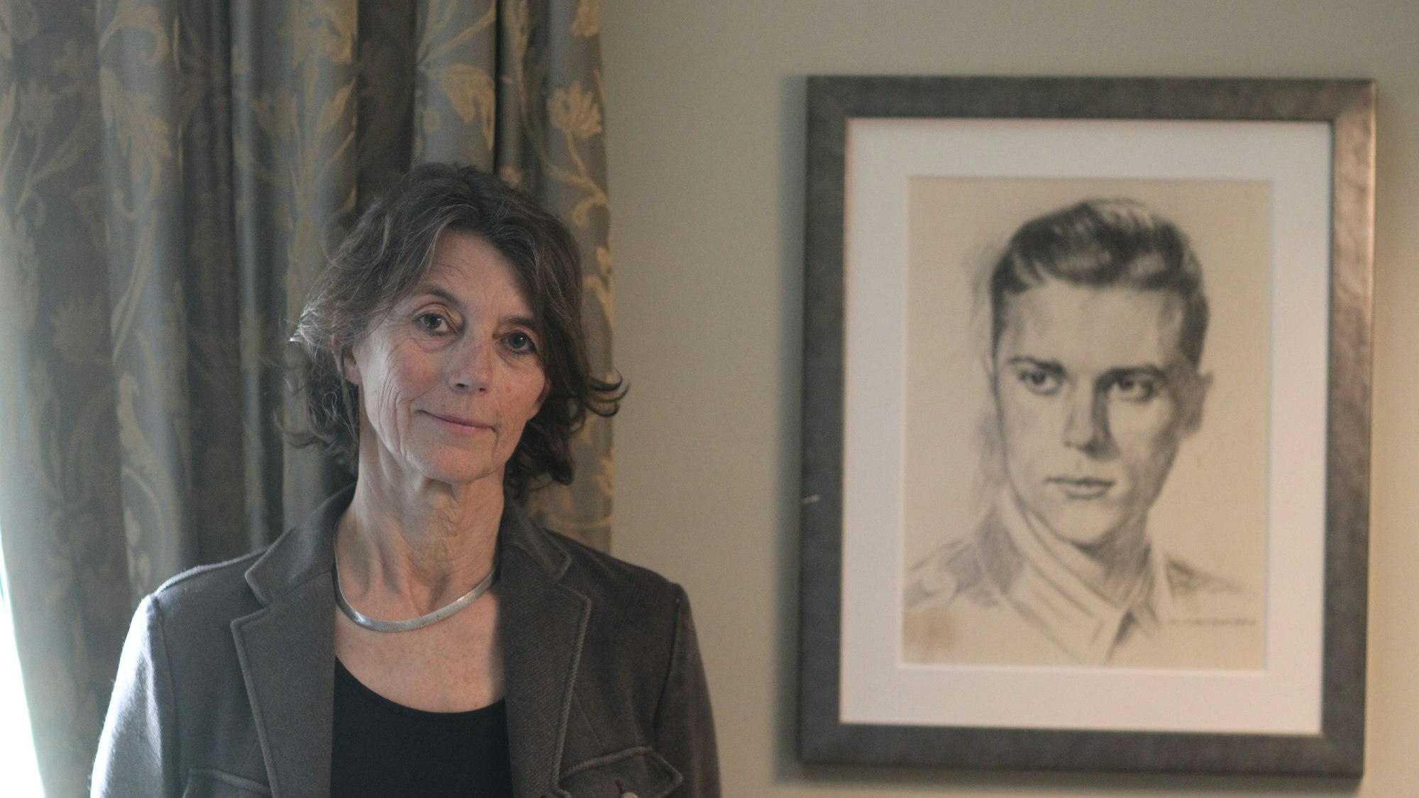 Eine Frau steht in einem Raum, an der Wand ein gezeichnetes Porträt