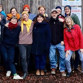 Vor einem hölzernen Tor in einer Ziegelmauer steht eine Gruppe Menschen.