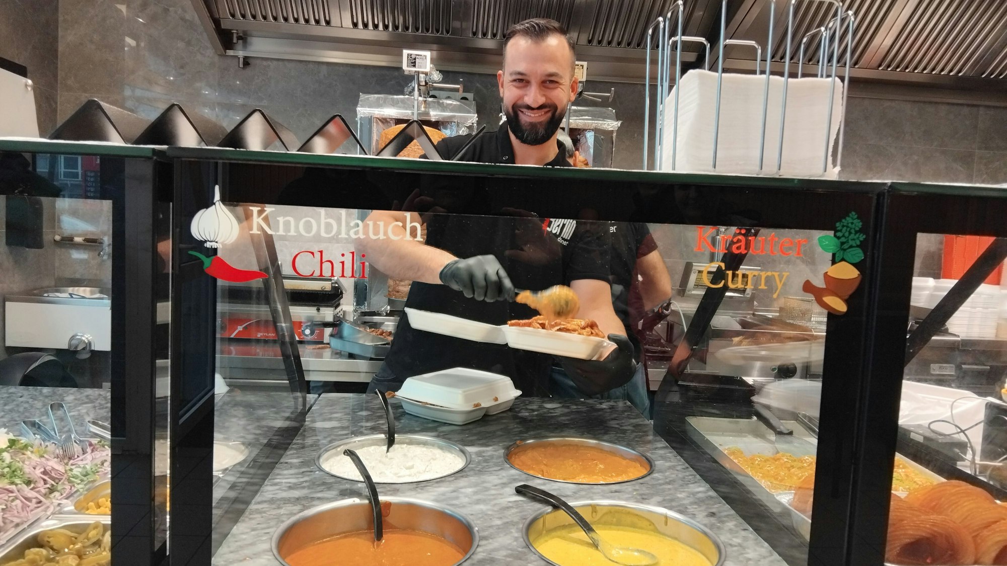 Ein Mann füllt Döner und Soße in eine Verpackung.