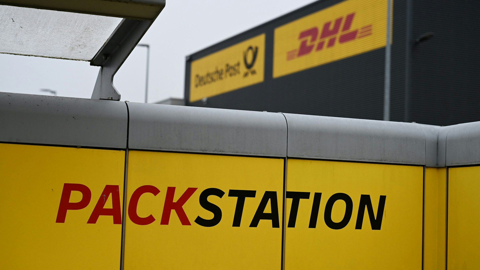 Der Schriftzug Packstation steht auf einem der DHL-Paketautomaten neben einer Zustellbasis des Bonner Logistikers.