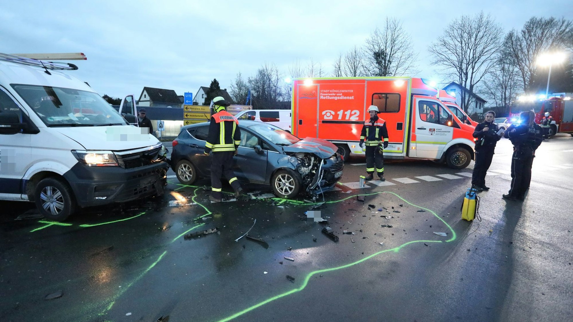 Feuerwehrleute und Polizisten stehen neben zwei beschädigten Fahrzeugen, im Hintergrund ein Rettungswagen