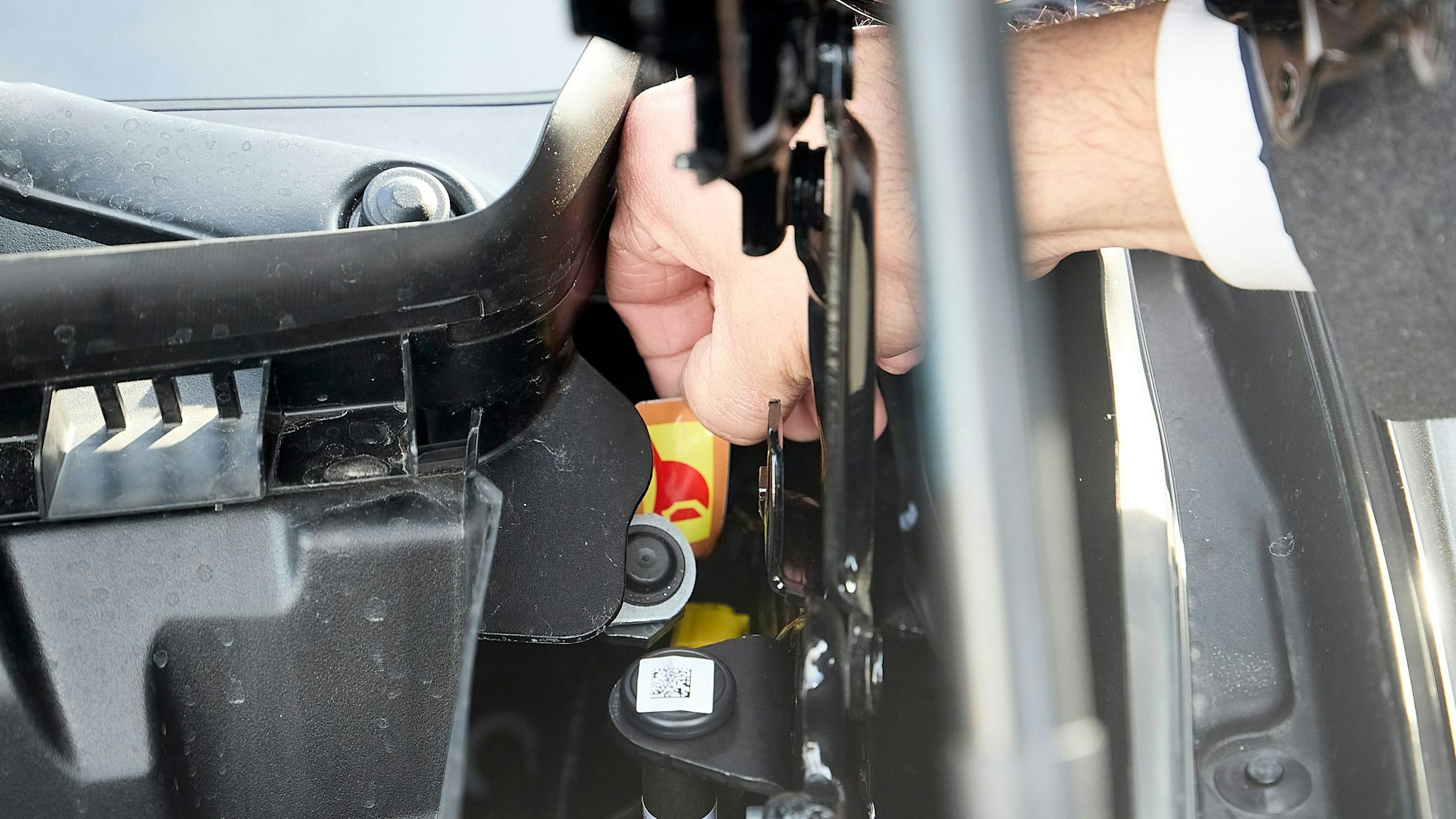 In einem engen Motorraum eines Elektrofahrzeugs greift ein Mann mit der rechten Hand nach dem zentralen Stecker.