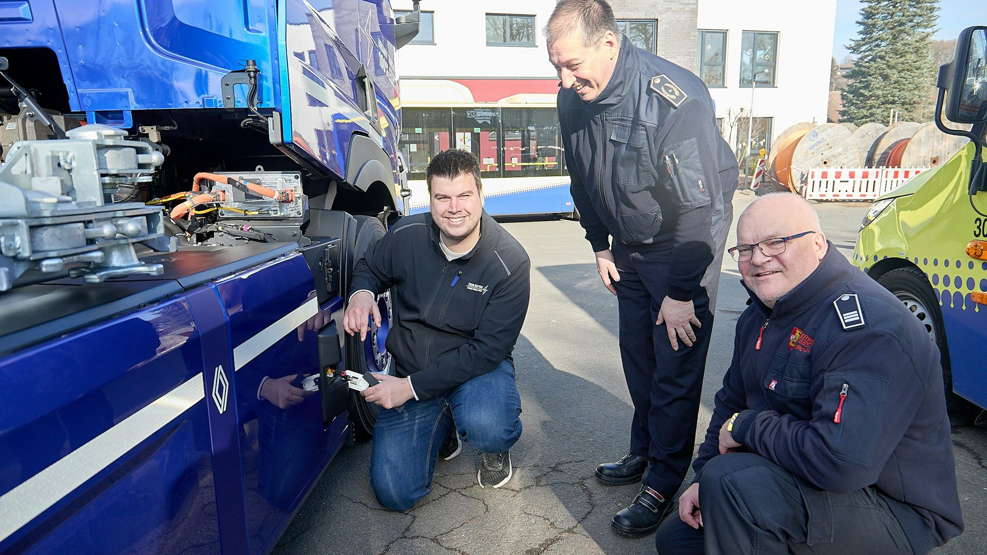 Drei Männer stehen an einem blauen Elektrofahrzeug und betrachten den Knopf zum Abschalten.