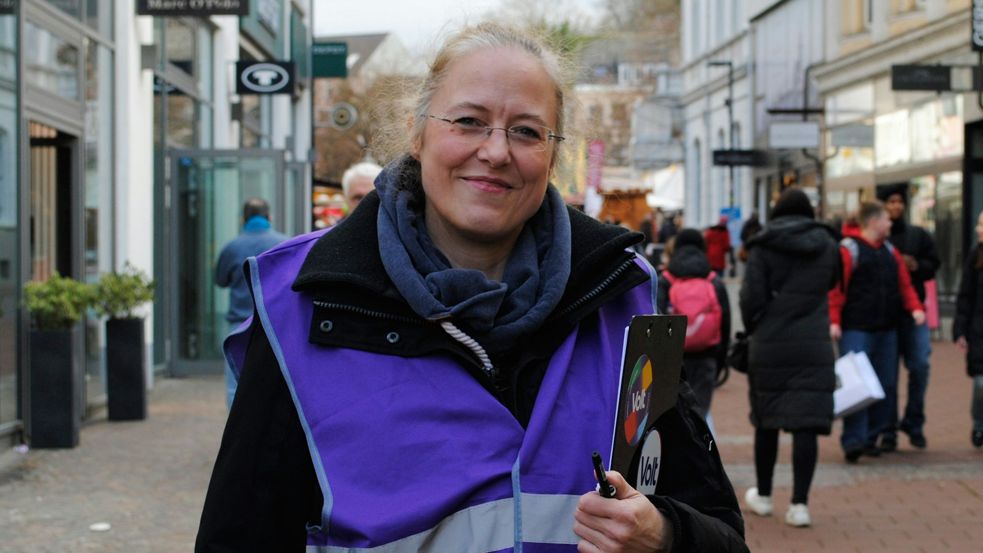 Eine Frau in Weste steht in einer Fußgängerzone.