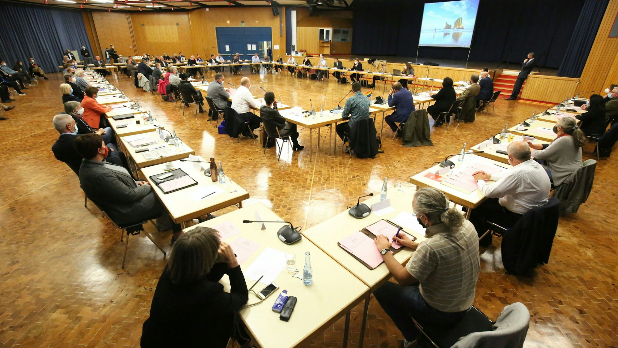52 Männer und Frauen sitzen an Tischen in der Aula des Schulzentrums Oberpleis
