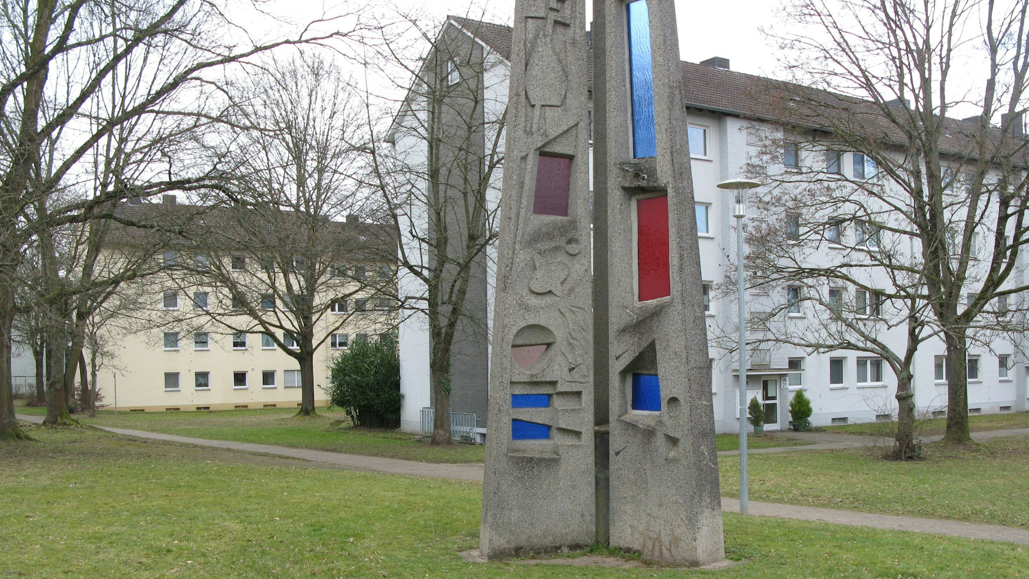 Ein Kunstwerk vor zwei Gebäuderiegeln mit Bäumen und Rasenflächen.