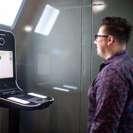 Das Bild zeigt einen Mann, der vor einem Gerät steht, das ein Foto aufnimmt.