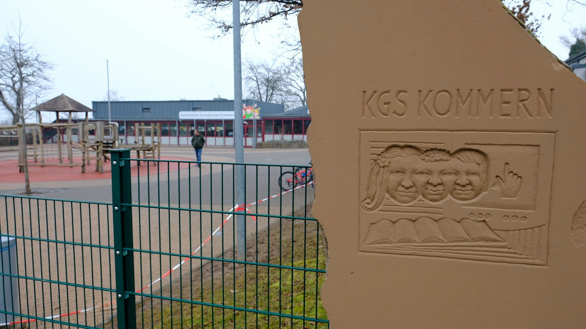 Neben dem Eingang zum Pausenhof der Katholischen Grundschule Kommern steht eine Sandsteinplastik mit der Aufschrift KGS Kommern.