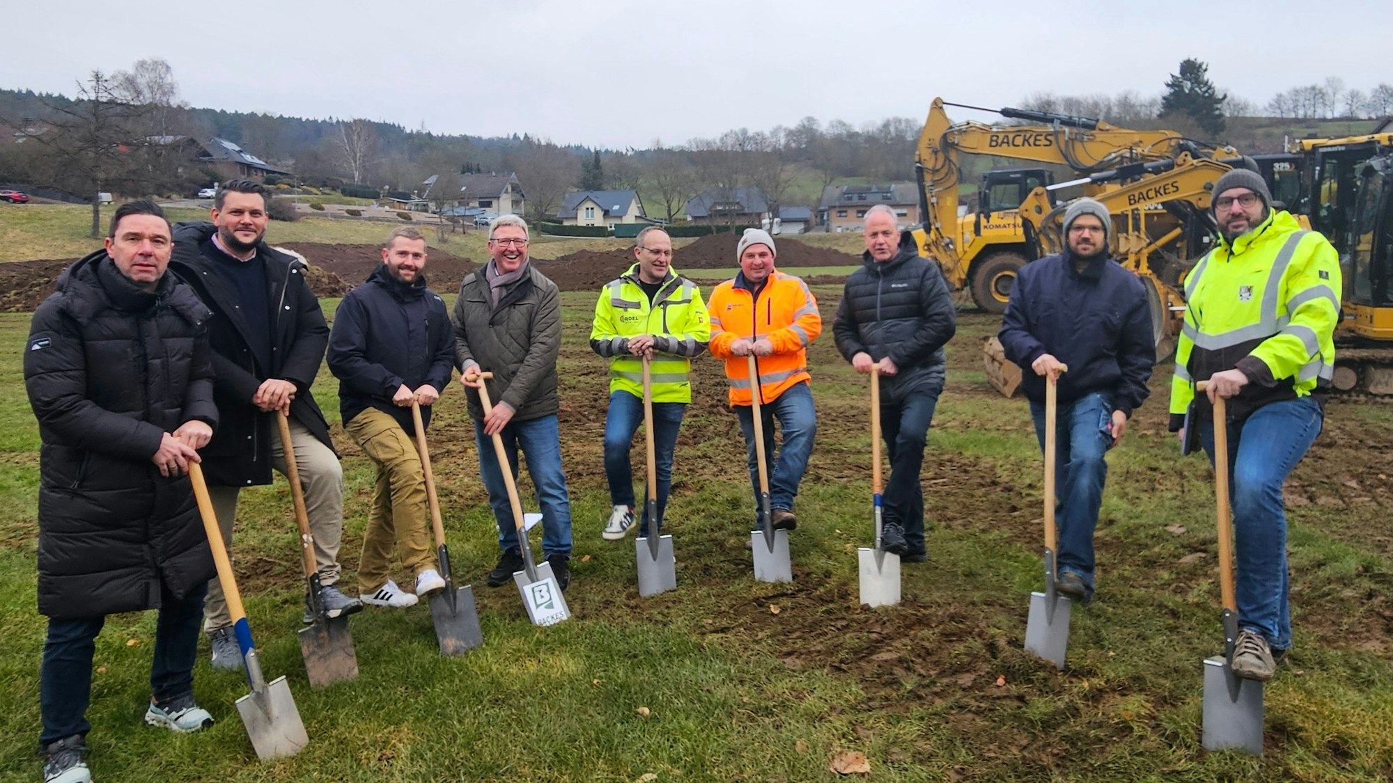 Neun Männer mit Spaten stehen in einem Halbkreis.