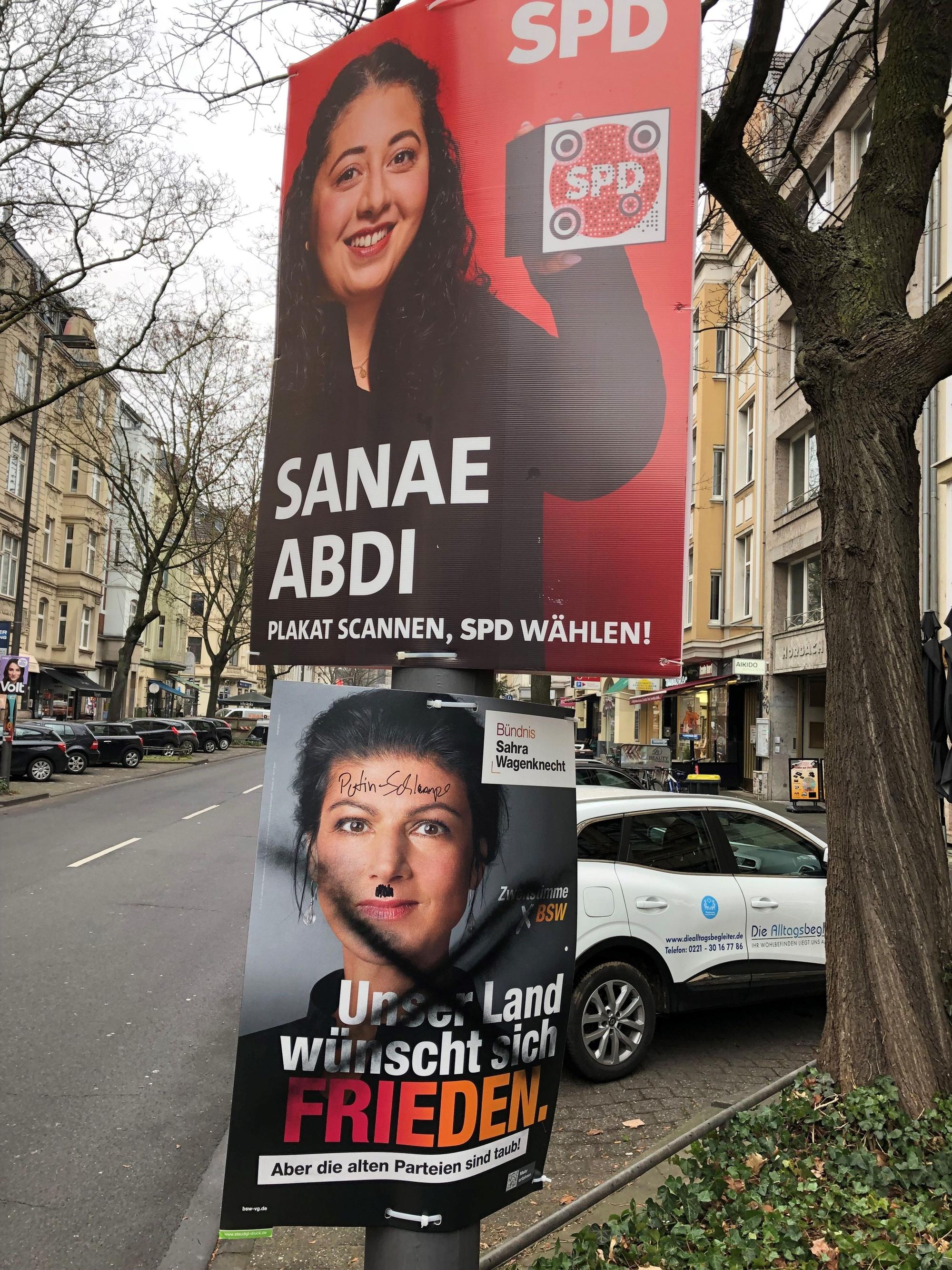 Ein von Unbekannten verunstaltetes Wahlplakat von Sarah Wagenknecht (BSW) hängt unter einem Plakat von Sanae Abdi (SPD) an der Neusser Straße in Köln.