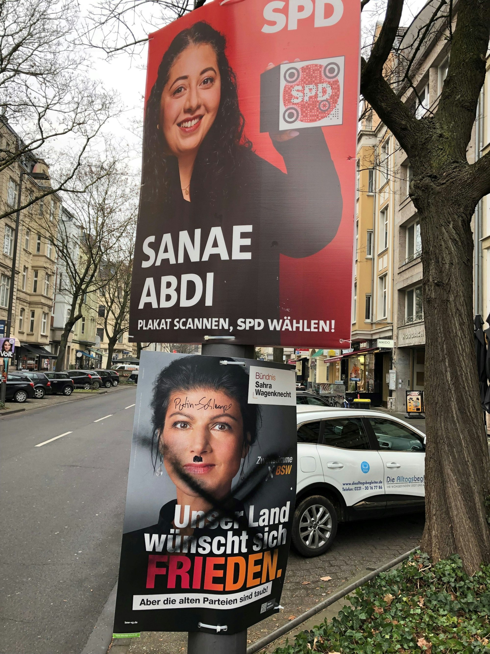 Ein von Unbekannten verunstaltetes Wahlplakat von Sarah Wagenknecht (BSW) hängt unter einem Plakat von Sanae Abdi (SPD) an der Neusser Straße in Köln.