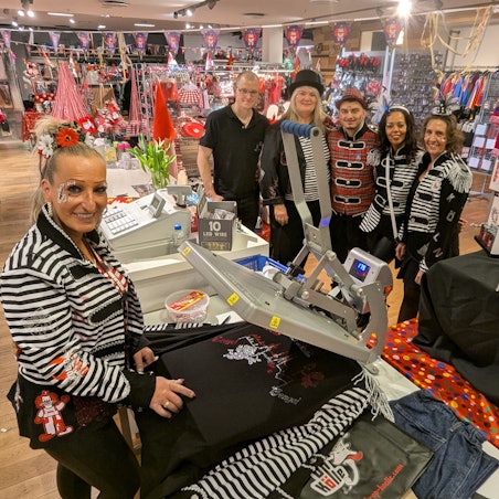 Tine Weckop an der Bügelpresse, dahinter ihr kostümiertes Team.