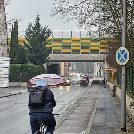 Ein Radfahrer hält einen Regenschirm und fährt eine Straße entlang.
