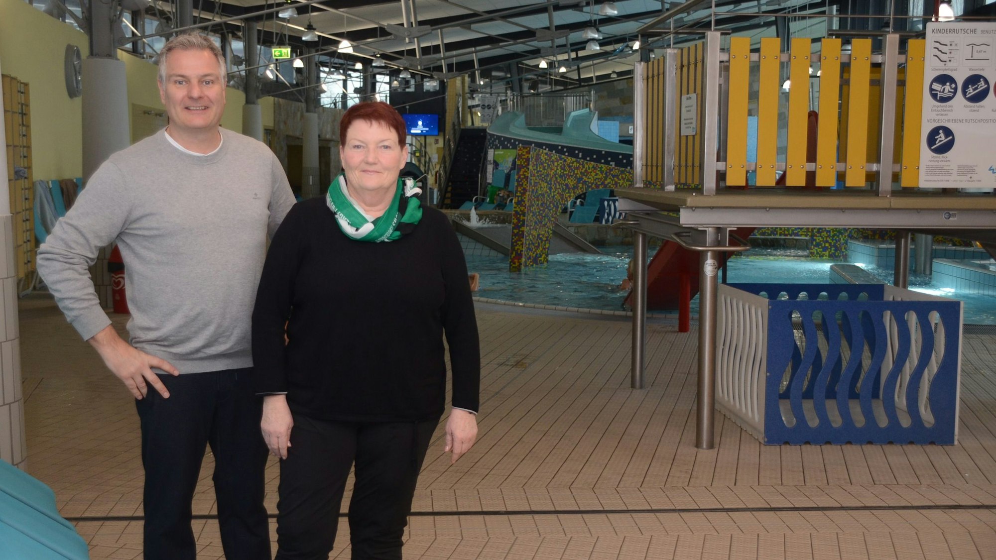 Ein Mann und eine Frau stehen in einem Hallenbad am Rand eines Kinderbeckens.