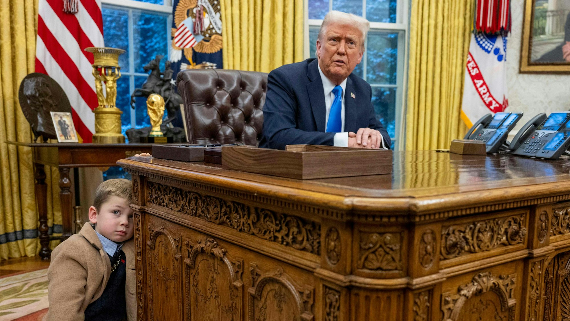 Elon Musks Sohn X Æ A-Xii lehnt am Schreibtisch von US-Präsident Donald Trump.