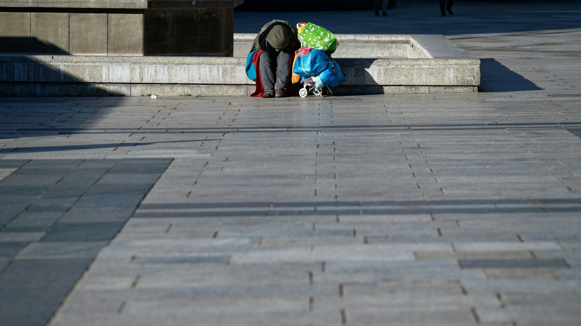 Köln: Ein Obdachloser wärmt sich auf dem Roncalliplatz vor dem Dom sitzend in der Sonne.