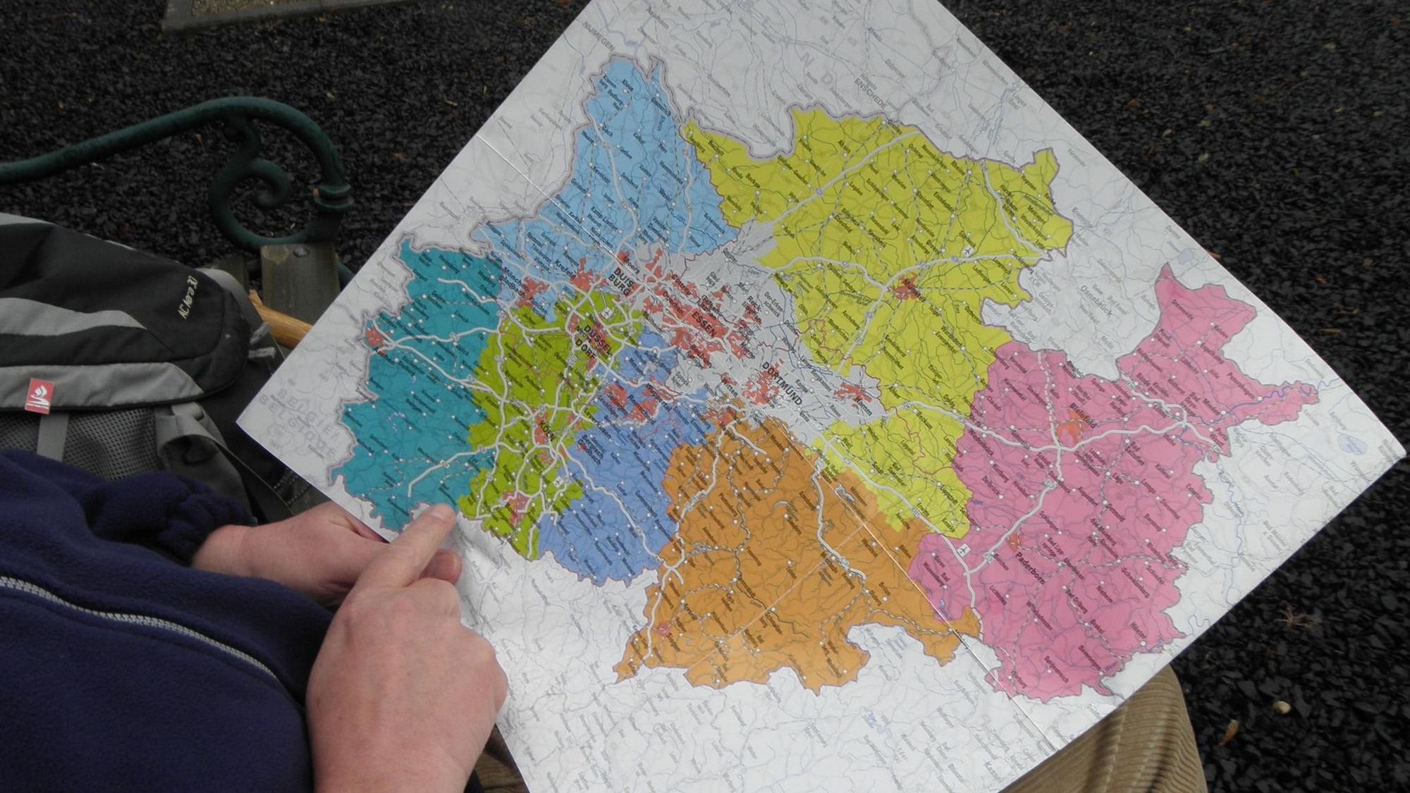 Ein Mann hält eine bunte Karte von Nordrhein-Westfalen in der Hand.