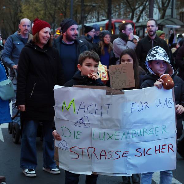 Viele Menschen sind an auf einer Straße unterwegs, zwei Kinder halten ein Plakat hoch mit dem Appell: Macht für uns die Luxemburger Straße sicher.