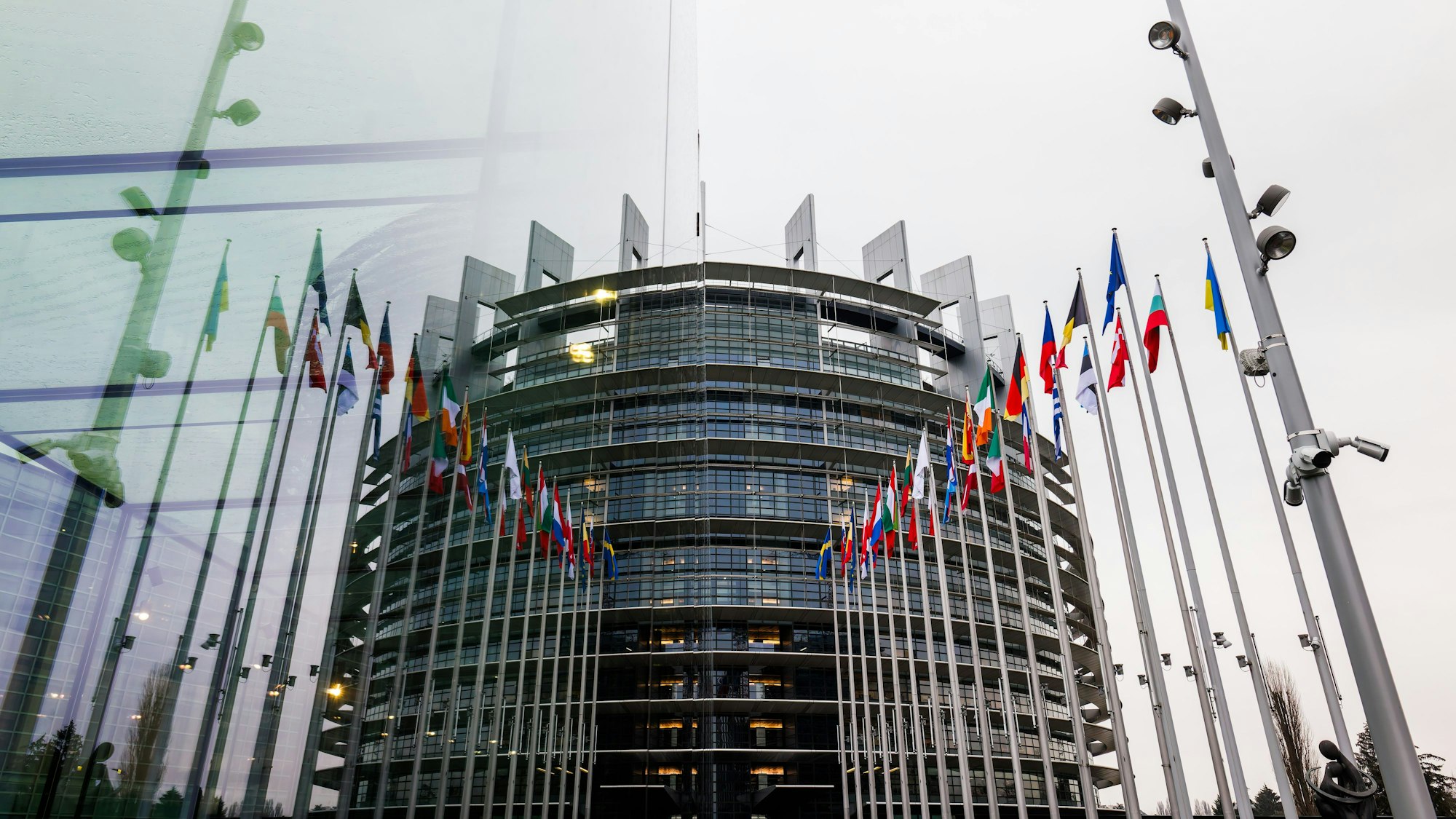 ARCHIV - 22.01.2025, Frankreich, Straßburg: Die Fahnen der Mitgliedsstaaten der Europäischen Union und der Ukraine wehen vor dem Gebäude des Europäischen Parlaments und spiegeln sich dabei in einer gläsernen Wand.