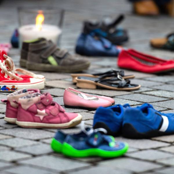 Verschiedene Schuhe von Kindern und Jugendlichen stehen auf dem Boden, dahinter ist eine Kerze zu sehen.