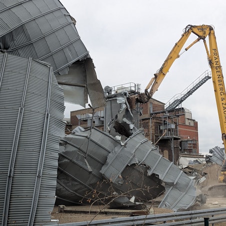 Das Foto zeigt einen Bagger, dessen Greifer ein altes Blechsilo auseinanderreißt.