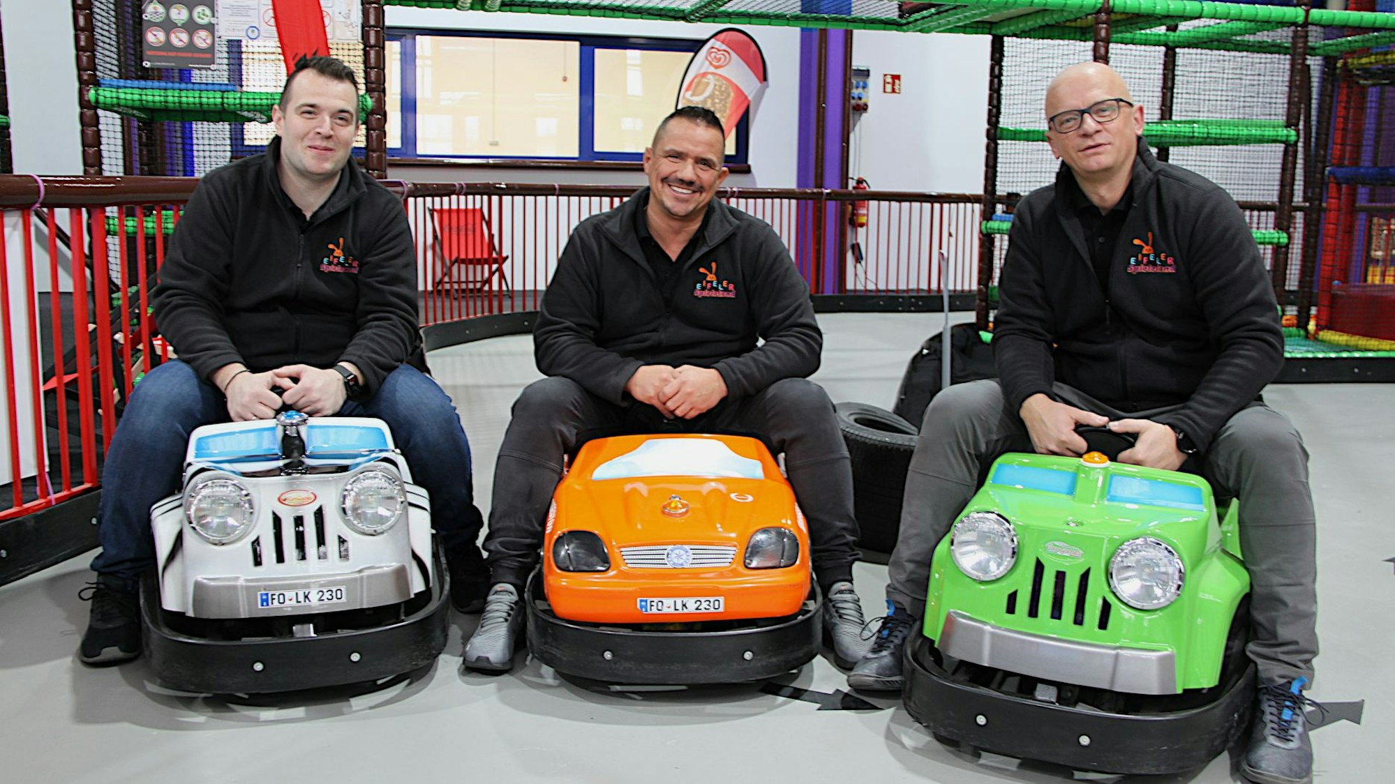 Drei Männer in schwarzen Pullovern sitzen im Eifeler Spieleland in Bad Münstereifel auf kleinen Elektro-Gokarts.
