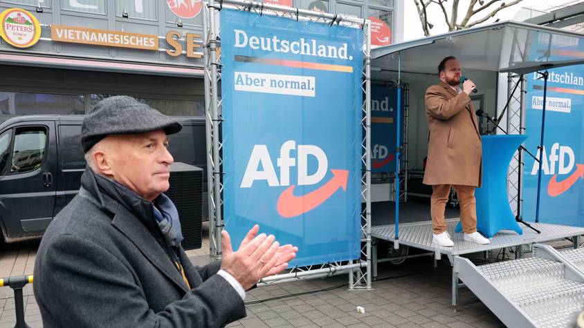 AfD-MdB Rüdiger Lucassen applaudiert neben einem Banner mit dem AfD-Emblem.