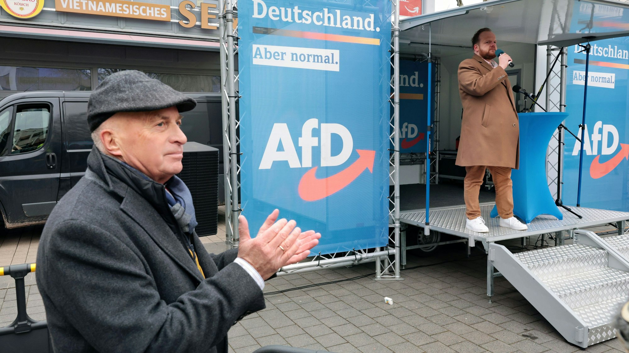 Der AfD-Bundestagsabgeordnete Rüdiger Lucassen steht neben einer Bühne, auf der Sven Tritschler spricht, und applaudiert.