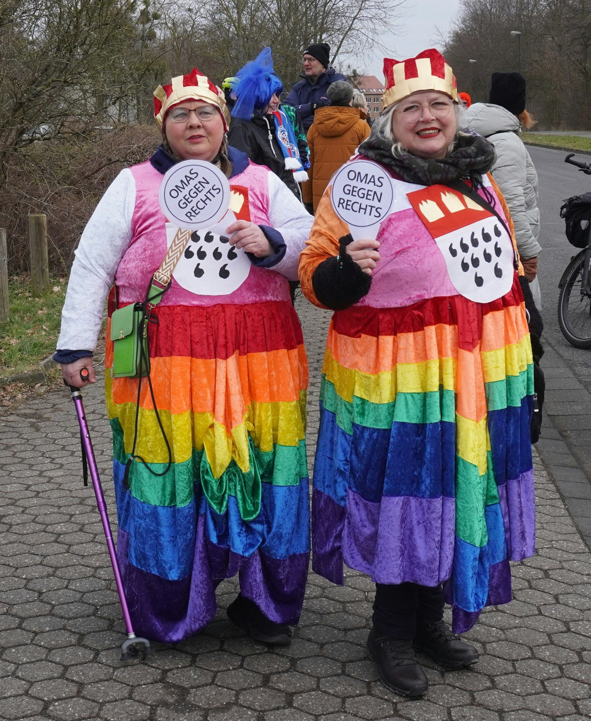 Auf dem Bild sind zwei ältere Damen in Regenbogenkostümen zu sehen.