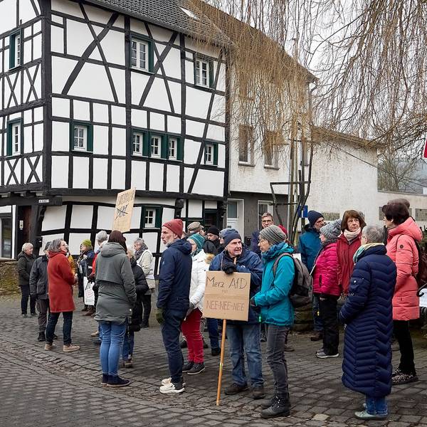 Auf dem Platz vor einem Fachwerkhaus stehen Menschen zu einer Mahnwache für die Demokratie zusammen. Manche tragen Schilder.