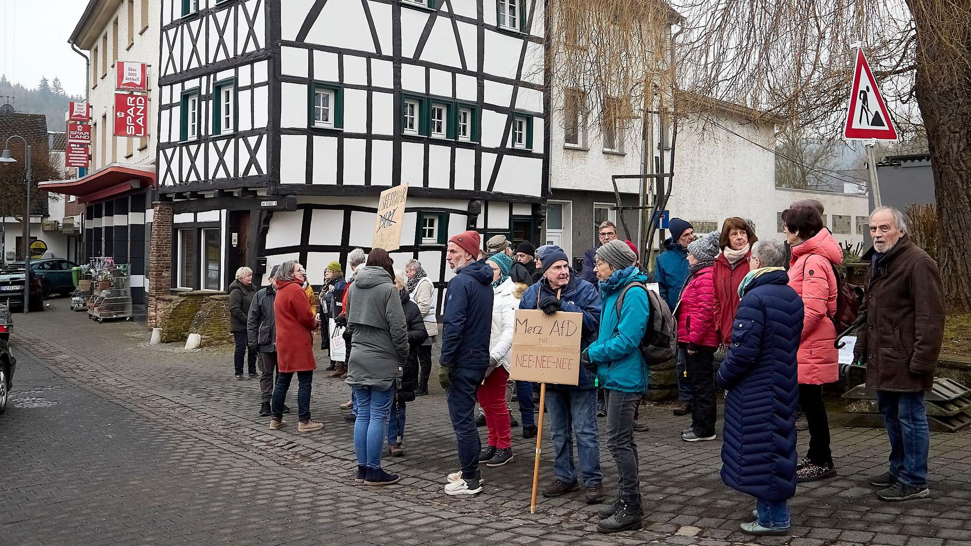 Auf dem Platz vor einem Fachwerkhaus stehen Menschen zu einer Mahnwache für die Demokratie zusammen. Manche tragen Schilder.