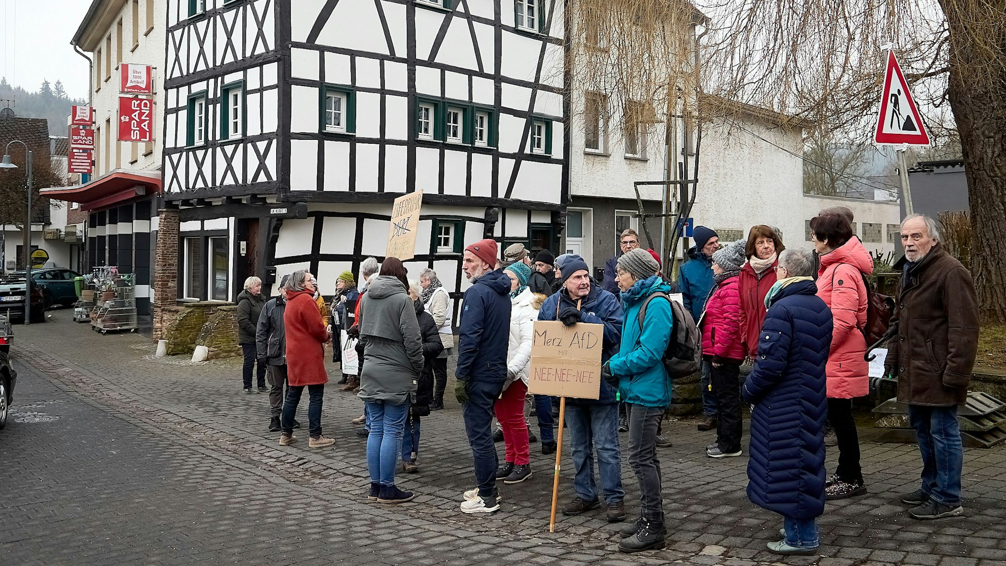 Auf dem Platz vor einem Fachwerkhaus stehen Menschen zu einer Mahnwache für die Demokratie zusammen. Manche tragen Schilder.