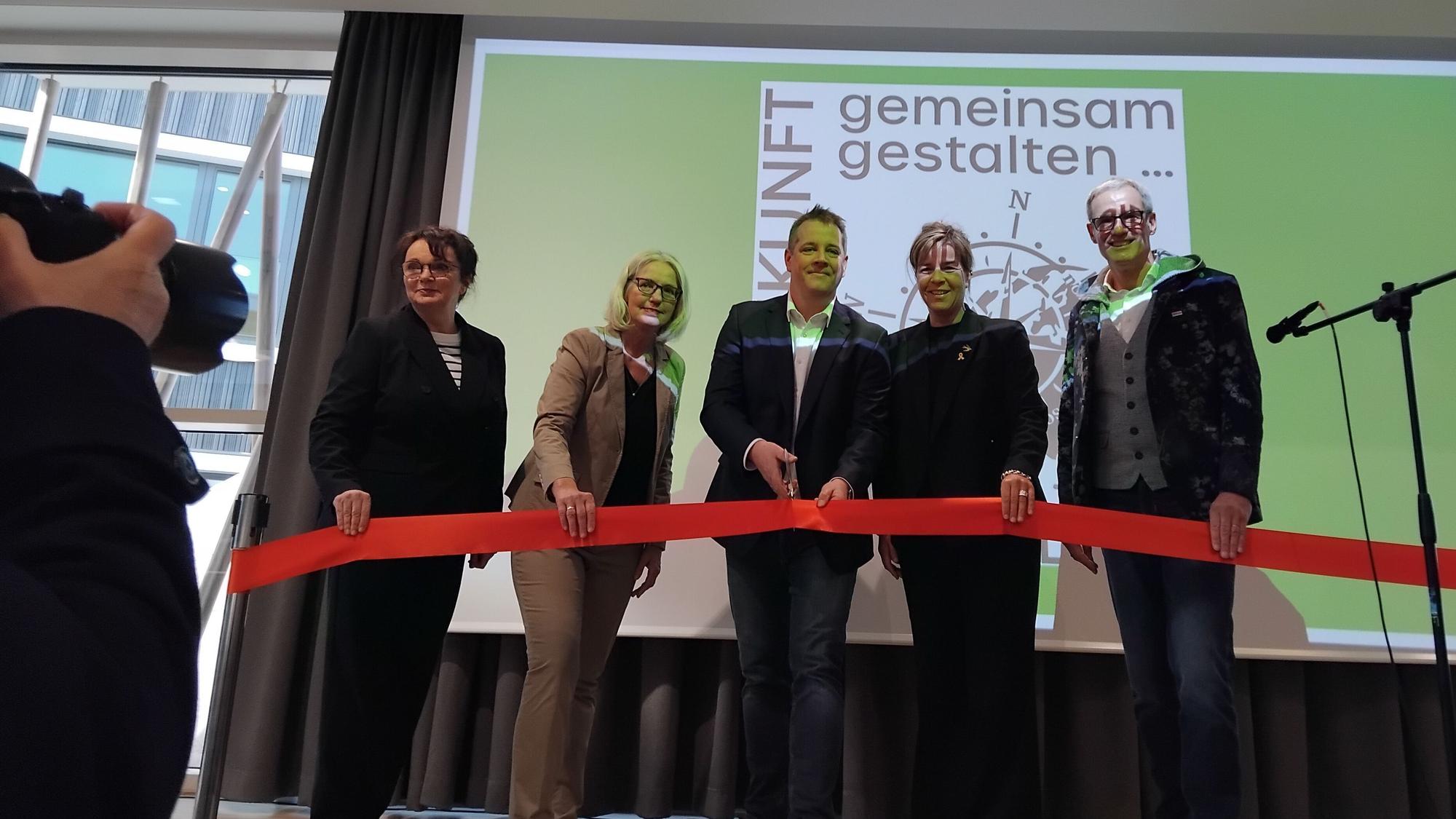 Fünf Personen durchschneiden auf einer Bühne ein rotes Band