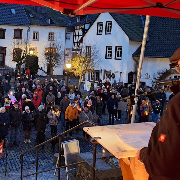 Ein Redner steht an einem Stehpult auf einer Bühne. Vor ihm auf dem Platz in Blankenheim stehen zahlreiche Menschen, von denen viele Kerzenlichter bei sich haben.