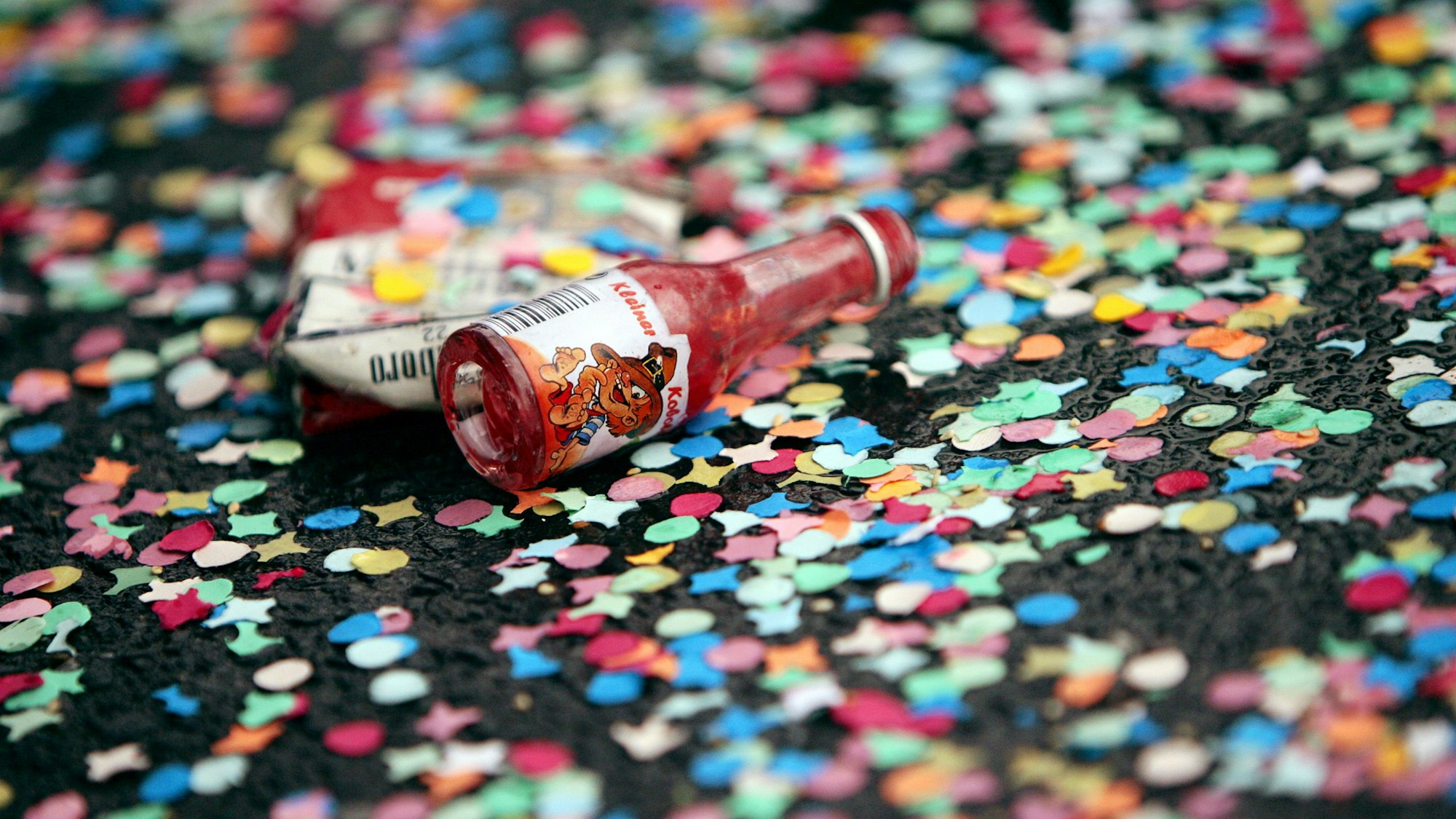 Ein leeres Schnapsfläschchen liegt auf der mit Konfetti übersäten Straße. (Archivbild)