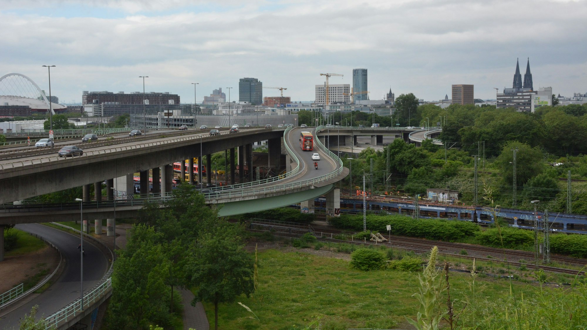 Blick auf die Stadtautobahn mit der Stadtsilhouette im Hintergrund und einer Grünfläche im Vordergrund