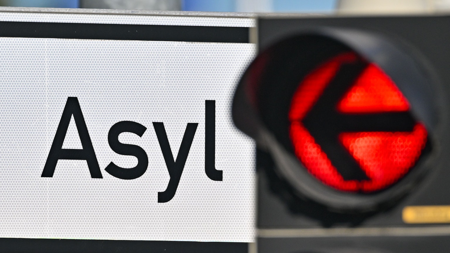 Eine rote Ampel leuchtet vor dem Wort „Asyl“ auf einem Wegweiser zur Erstaufnahme-Einrichtungen (EAE) (Symbolbild)
