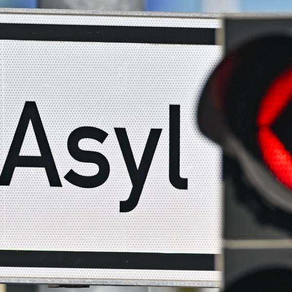 Eine rote Ampel leuchtet vor dem Wort „Asyl“ auf einem Wegweiser zur Erstaufnahme-Einrichtungen (EAE) (Symbolbild)