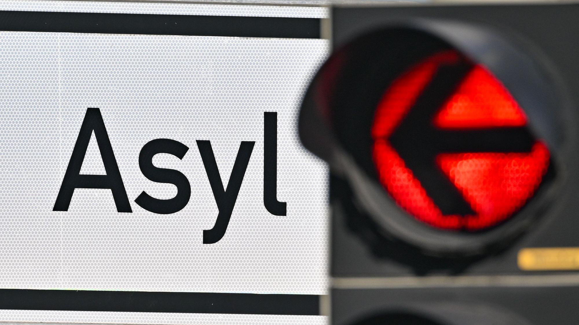 Eine rote Ampel leuchtet vor dem Wort „Asyl“ auf einem Wegweiser zur Erstaufnahme-Einrichtungen (EAE) (Symbolbild)