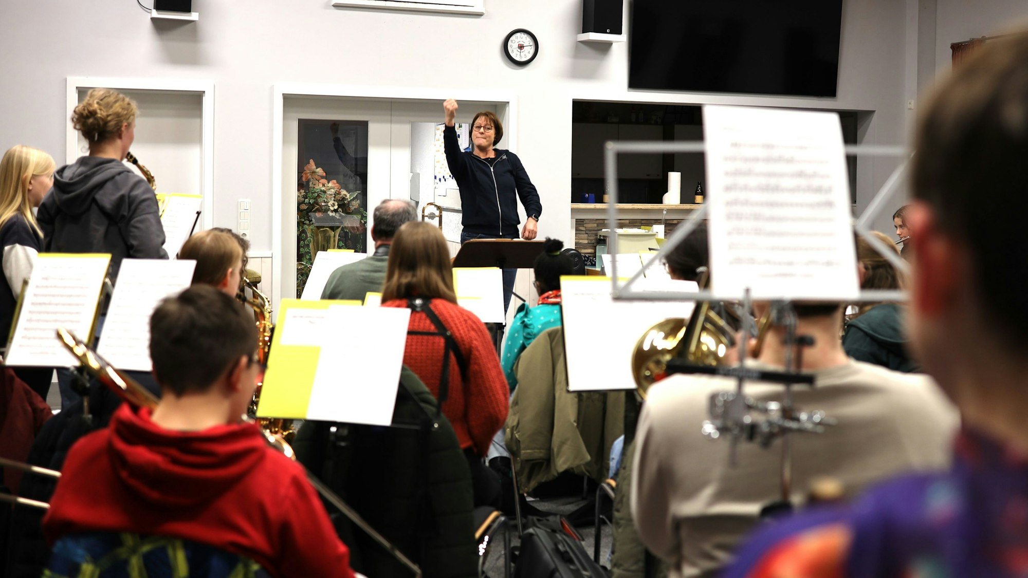 Orchesterleiterin Andrea Cosman steht im Musikheim am Dirigentenpult und dirigiert die jungen Musikerinnen und Musiker, die vor ihr sitzen.