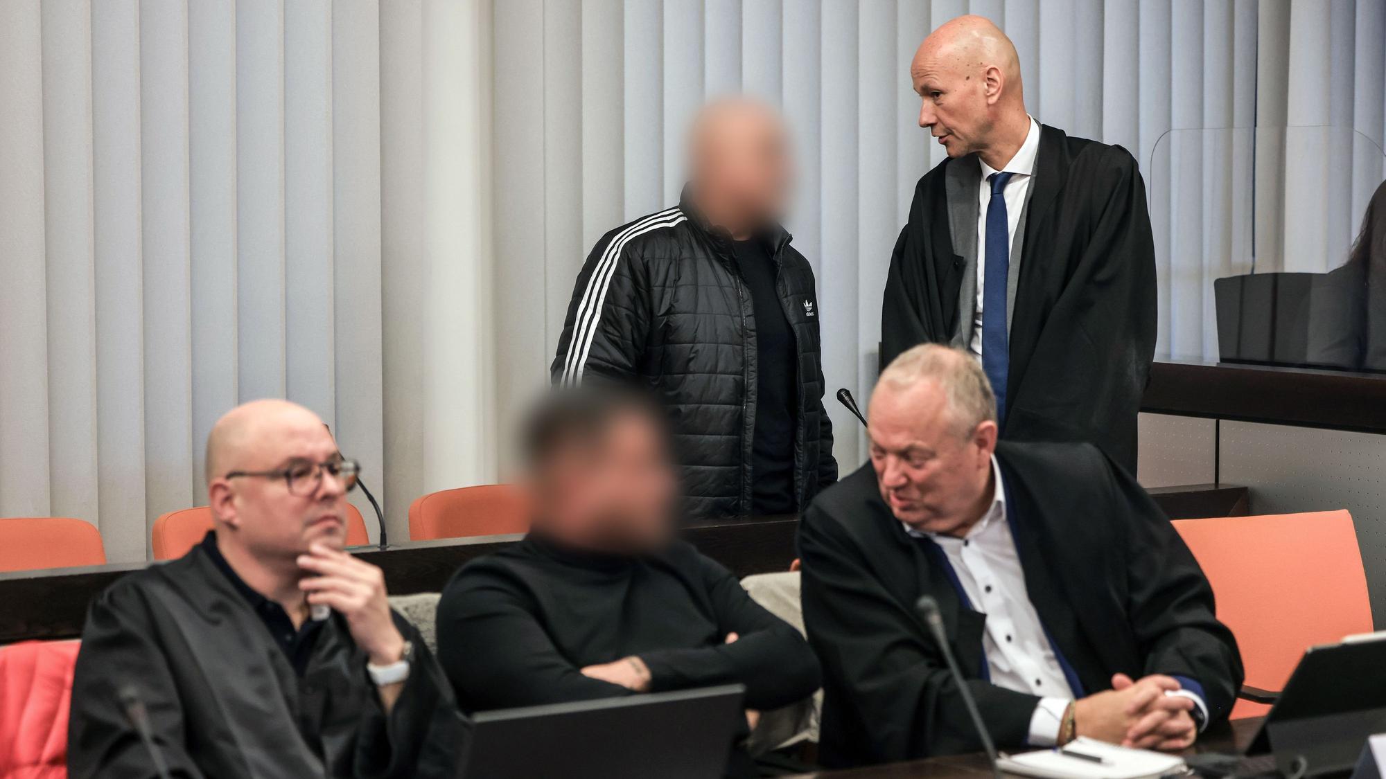 Der Hauptangeklagte (hinten, links) spricht im Gerichtssaal mit seinem Verteidiger Oliver Doelfs (hinten, rechts), während vorne ein Angeklagter (M) mit seinem Verteidiger Hartmut Moyzio (vorne, rechts) spricht.